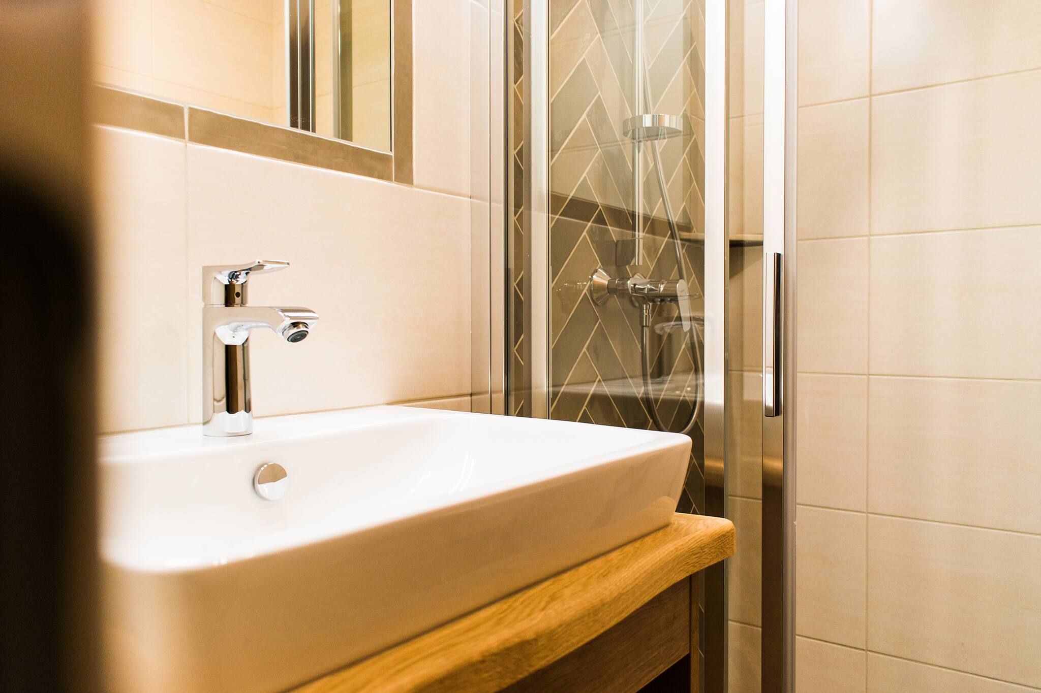 Une salle de bain avec un lavabo blanc, un miroir et un espace douche doté d’une porte en verre.