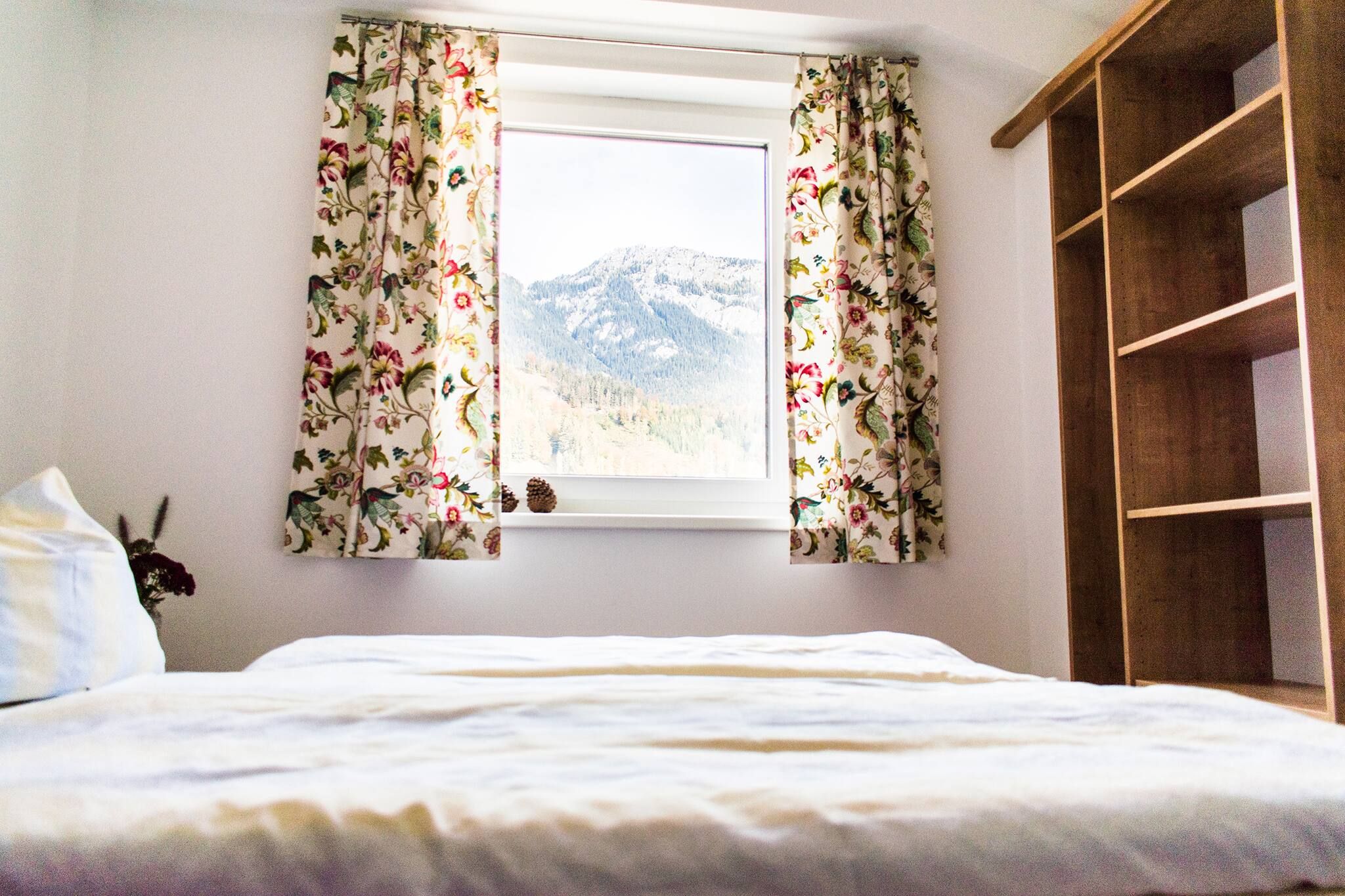 Une chambre à coucher avec un lit, une fenêtre ornée de rideaux à motifs floraux et une armoire en bois.