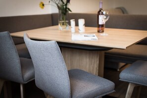 Ein Essbereich mit einem Holztisch, grau gepolsterten Stühlen, einer Vase mit einer gelben Blume und einer Weinflasche.