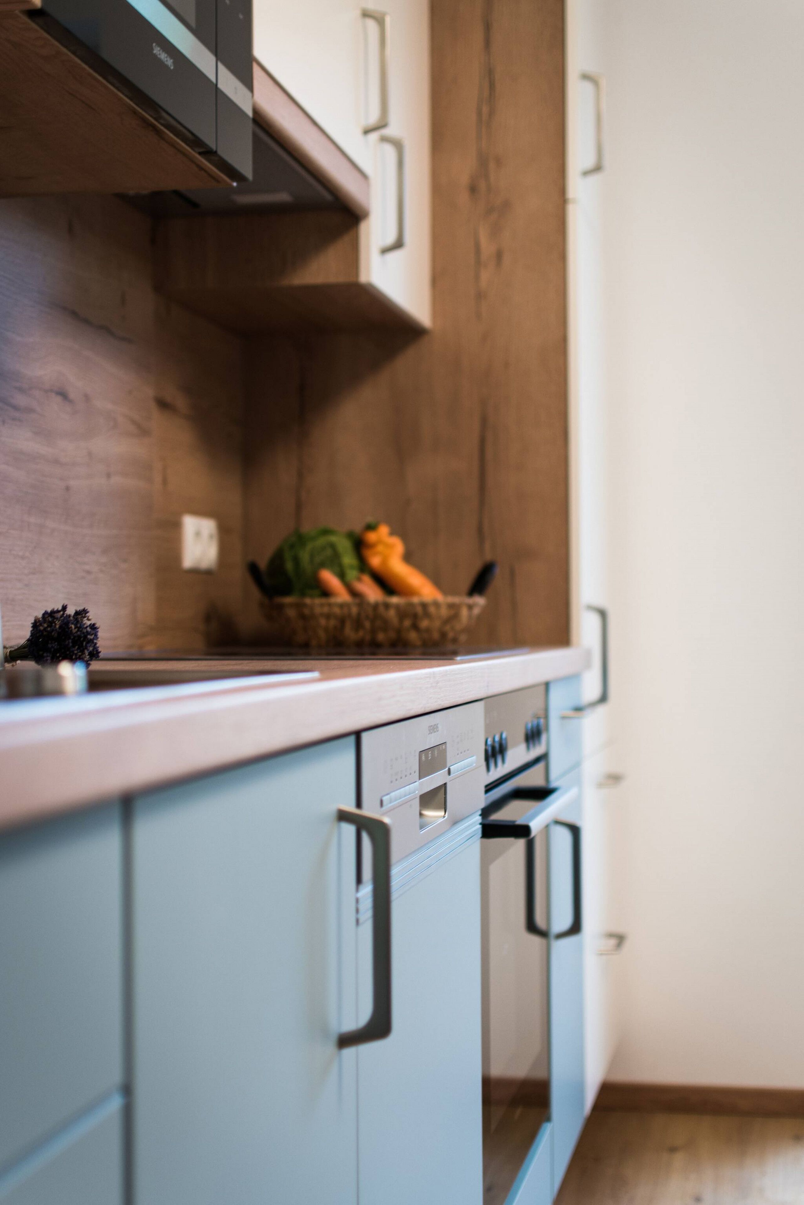 Une cuisine avec un plan de travail en bois, un panier de légumes et un four encastré.