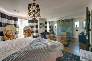 Ett sovrum med en stor säng, en sittgrupp med soffa och fåtöljer, en accentvägg i sten och en kristallkrona.