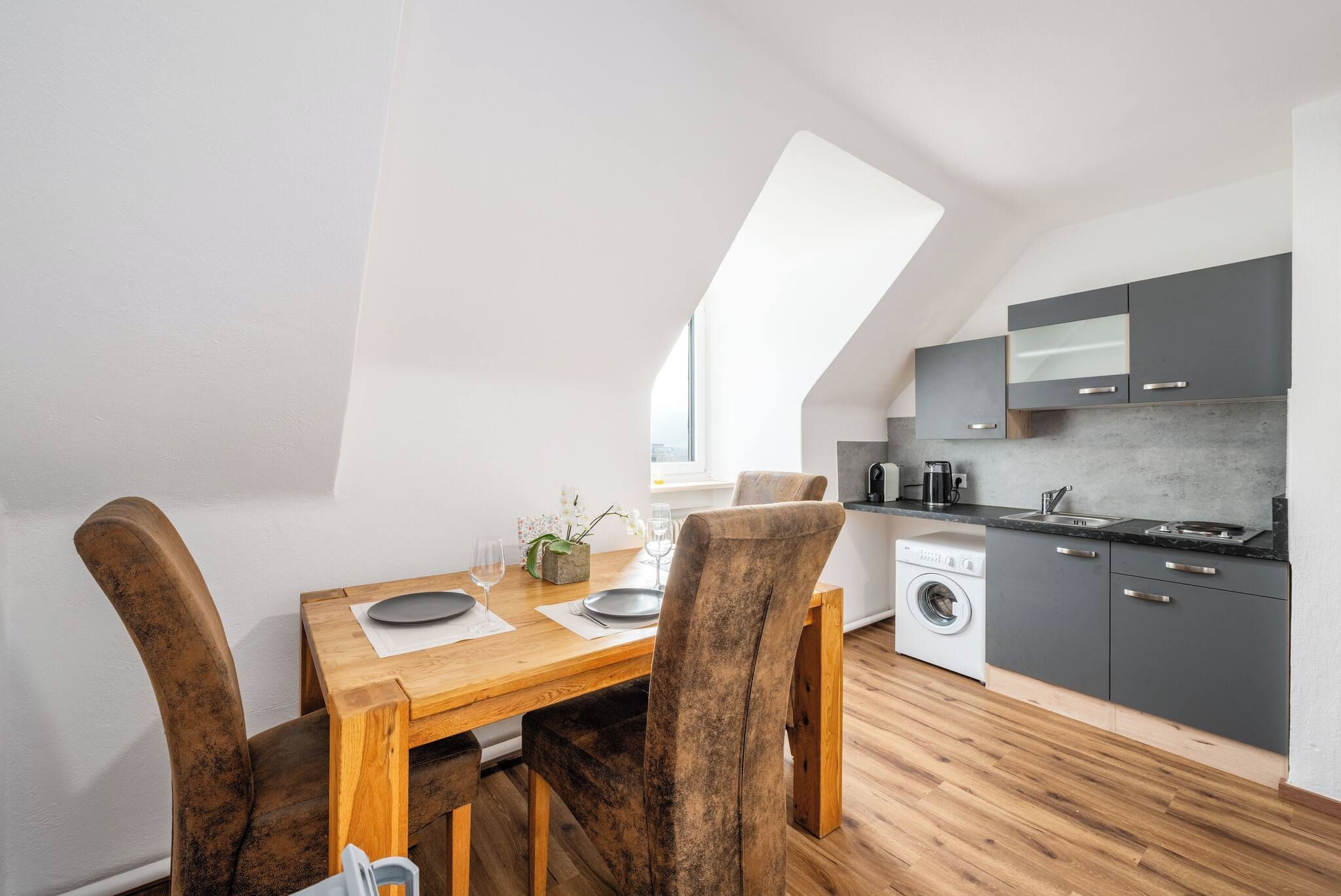 Een compacte keuken met moderne apparatuur, een eethoek met houten meubels, en een dakraam.