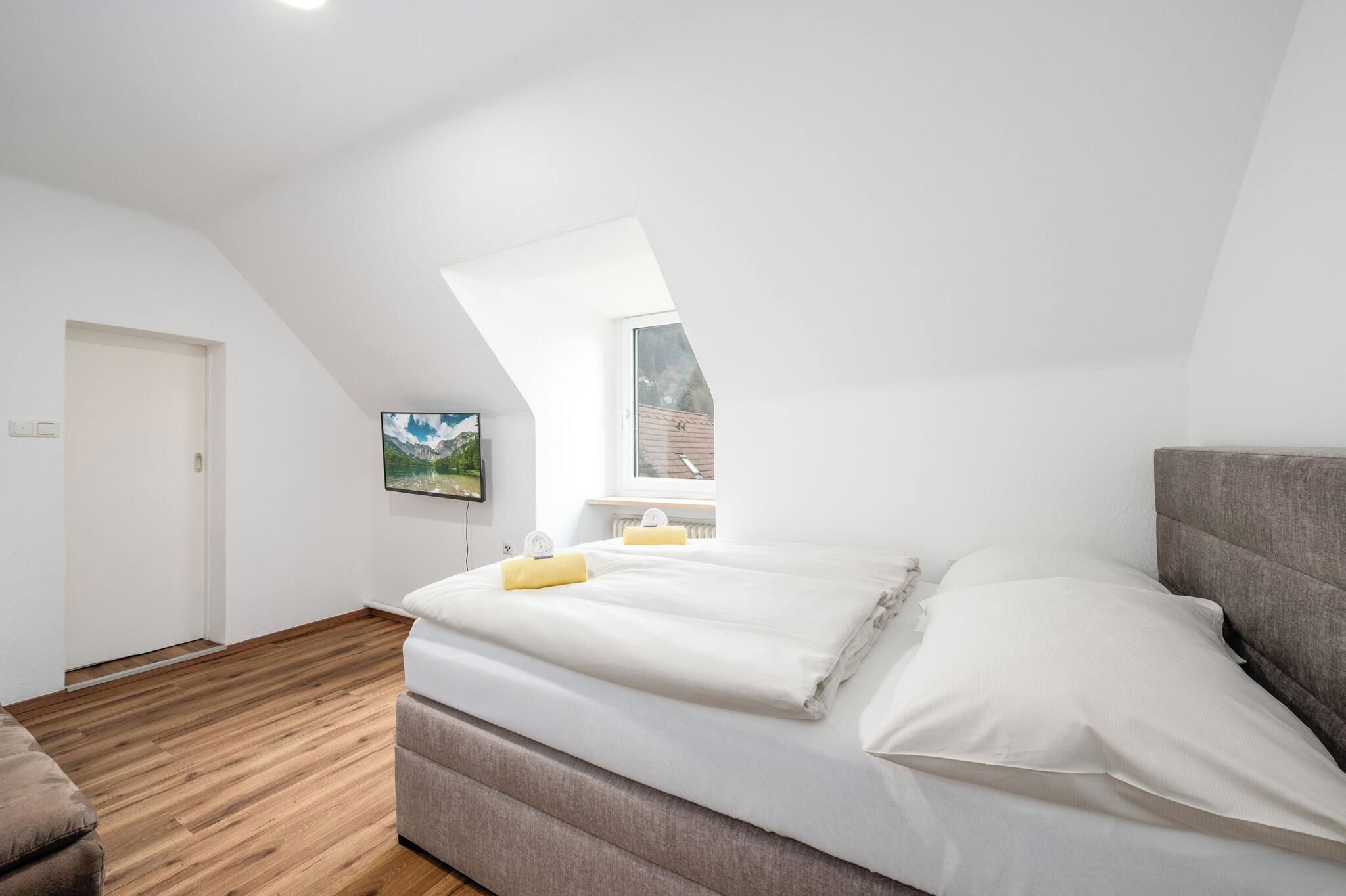 Una camera da letto con soffitto spiovente, un letto, una finestra e una TV a parete.