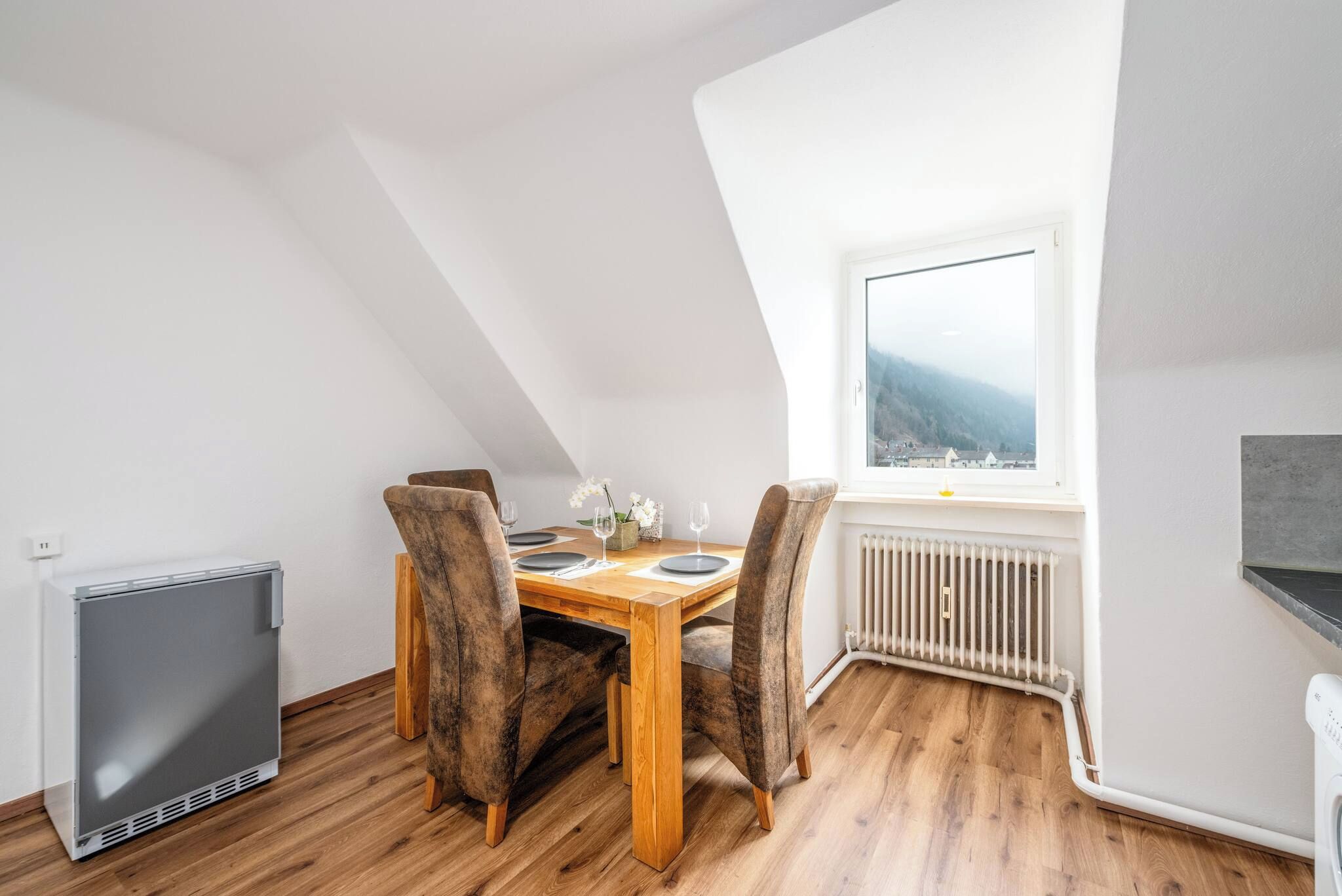 Zona pranzo con tavolo in legno, due sedie, un termosifone e una finestra vista.