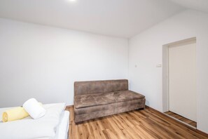 A small, sparsely furnished room with a wooden floor, a brown sofa, and a bed with white bedding. - EasyStay Apartment Top 9 (Liezen)