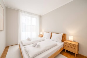 A hotel room with a double bed, two bedside tables with lamps, a large window with sheer curtains, and a wooden floor. - Mountain Paradise - Grimming 1 (Gröbming)