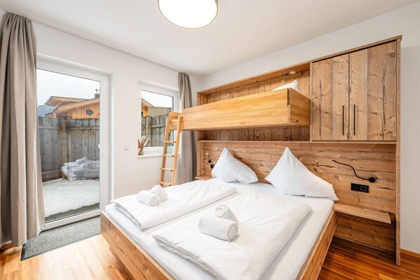 A hotel room with a wooden headboard, a double bed with white linens, a wooden wardrobe, and a sliding glass door leading to an outdoor area. - Mountain Soulscape 1 (Haus im Ennstal)