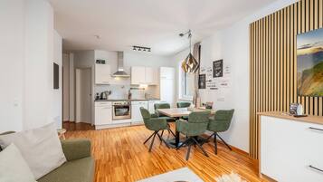 Une cuisine moderne avec des meubles blancs, un coin repas avec une table en bois et des chaises vertes, et un salon avec un canapé vert.