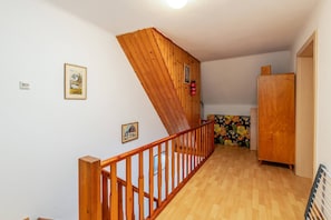 Una scala in legno con ringhiera conduce a una stanza con un divano a motivi floreali e un armadio in legno.