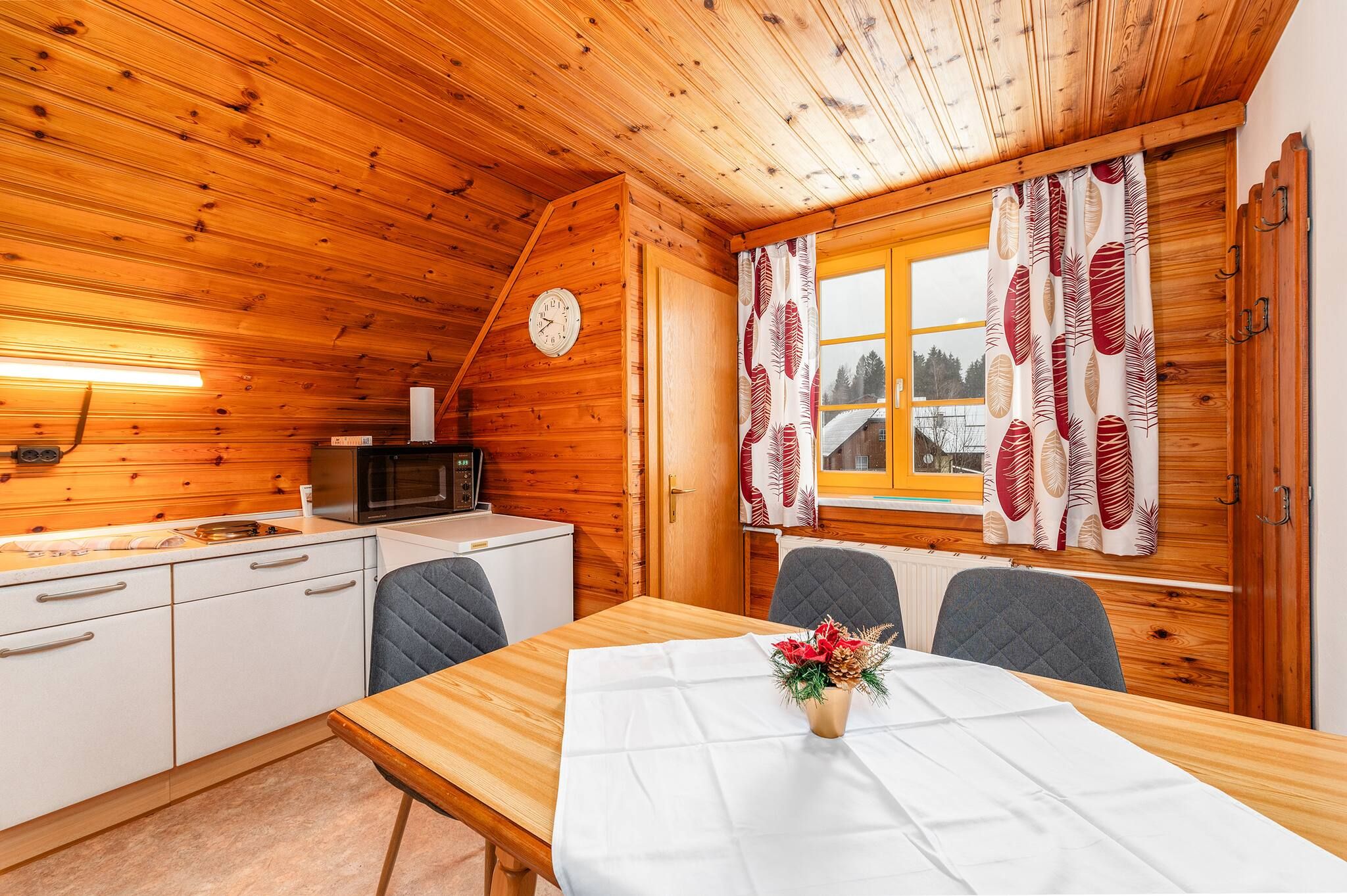 Ein gemütliches Blockhaus-Interieur mit Holzvertäfelung, einem Esstisch mit weißer Tischdecke und einer Uhr an der Wand.
