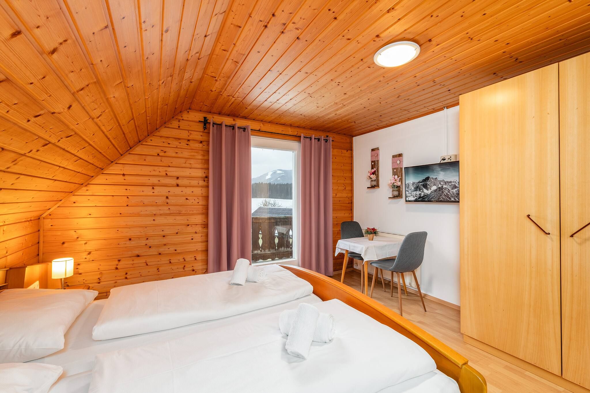 Een kamer met houten lambrisering, twee bedden, een eettafel en een televisie.