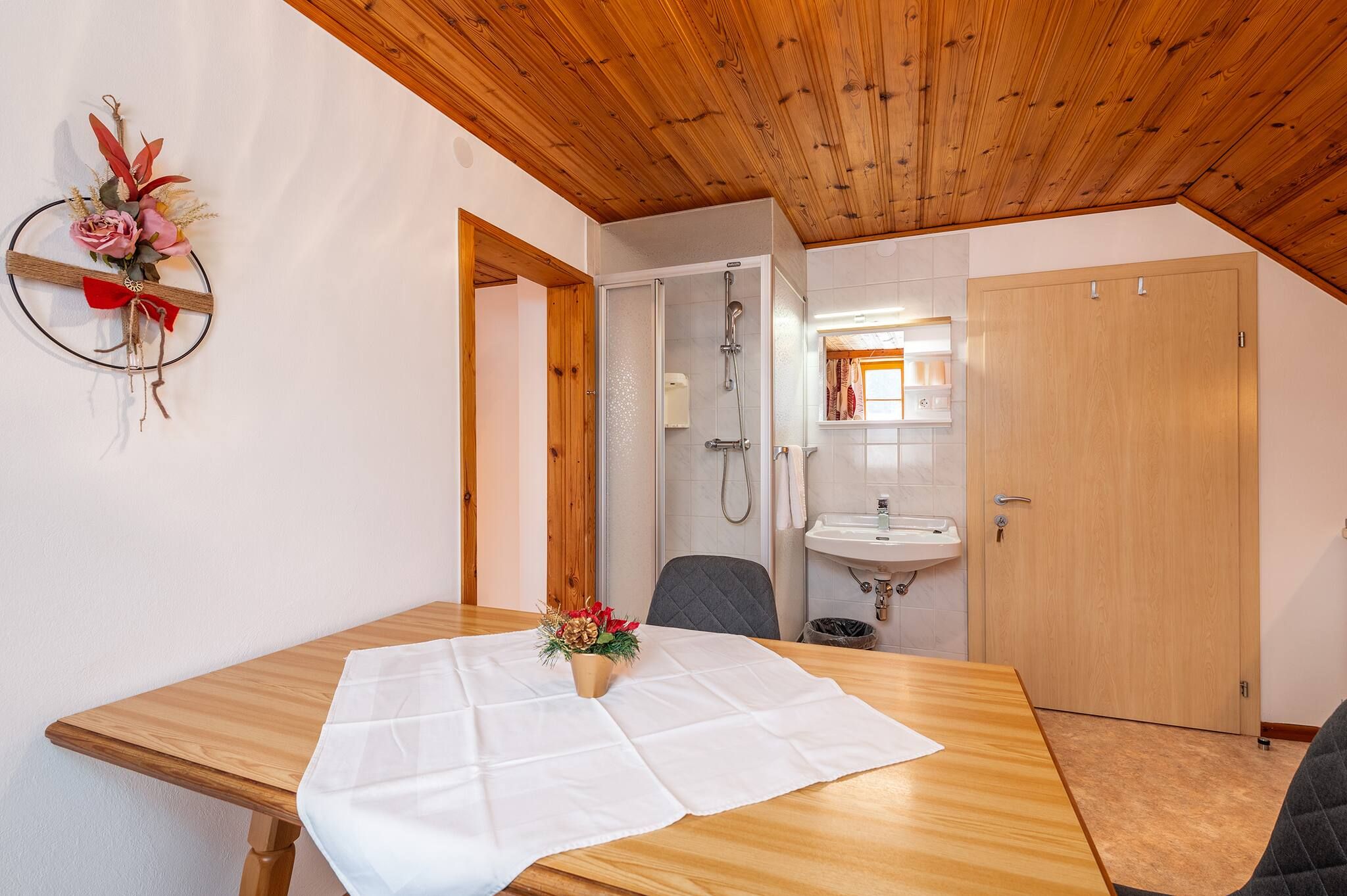 Ein Zimmer mit einem Holztisch, einer Dusche, einem Waschbecken und einer Tür.