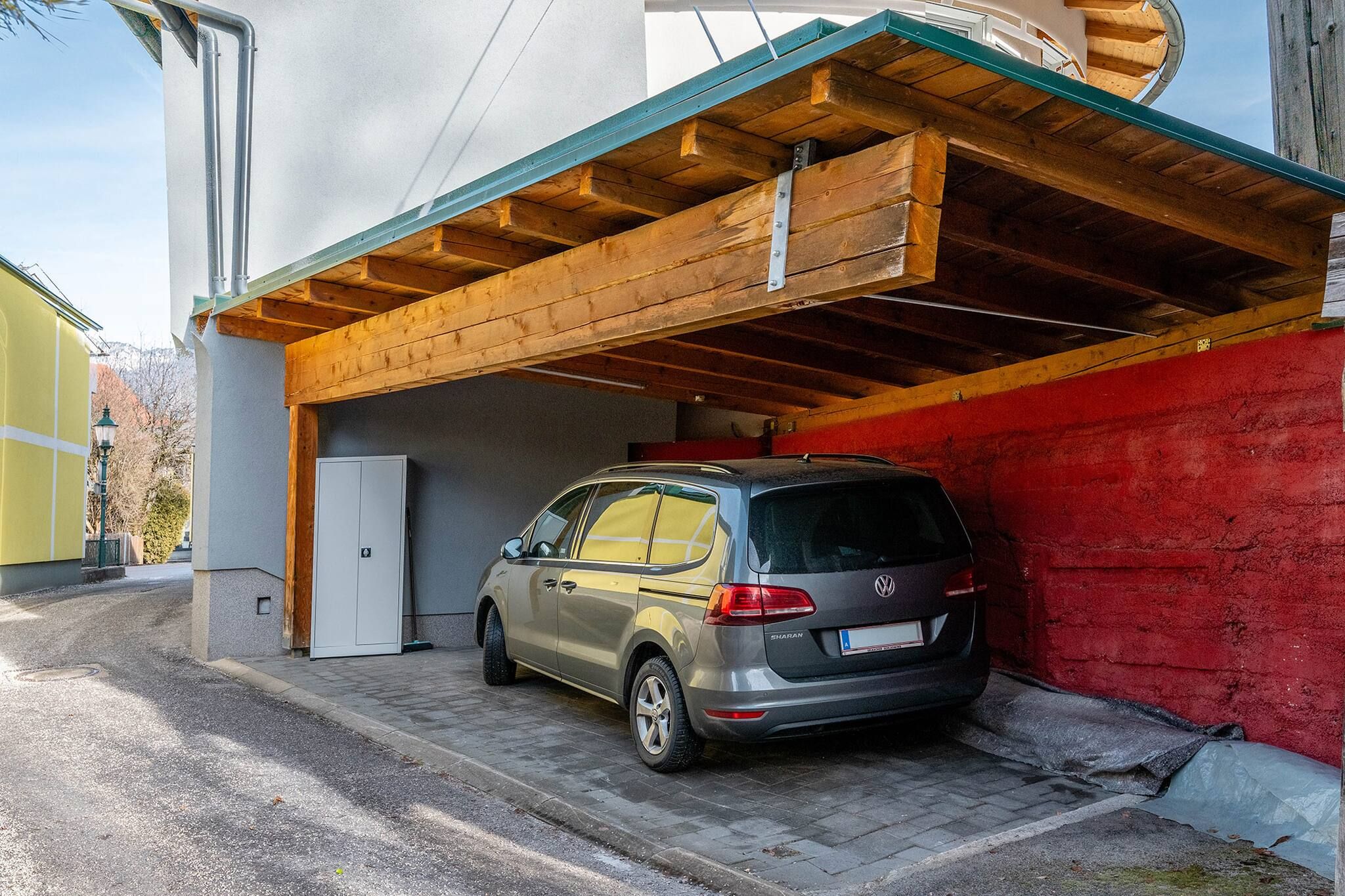 Un Volkswagen Sharan plateado estacionado en un garaje con techo de madera y pared roja.