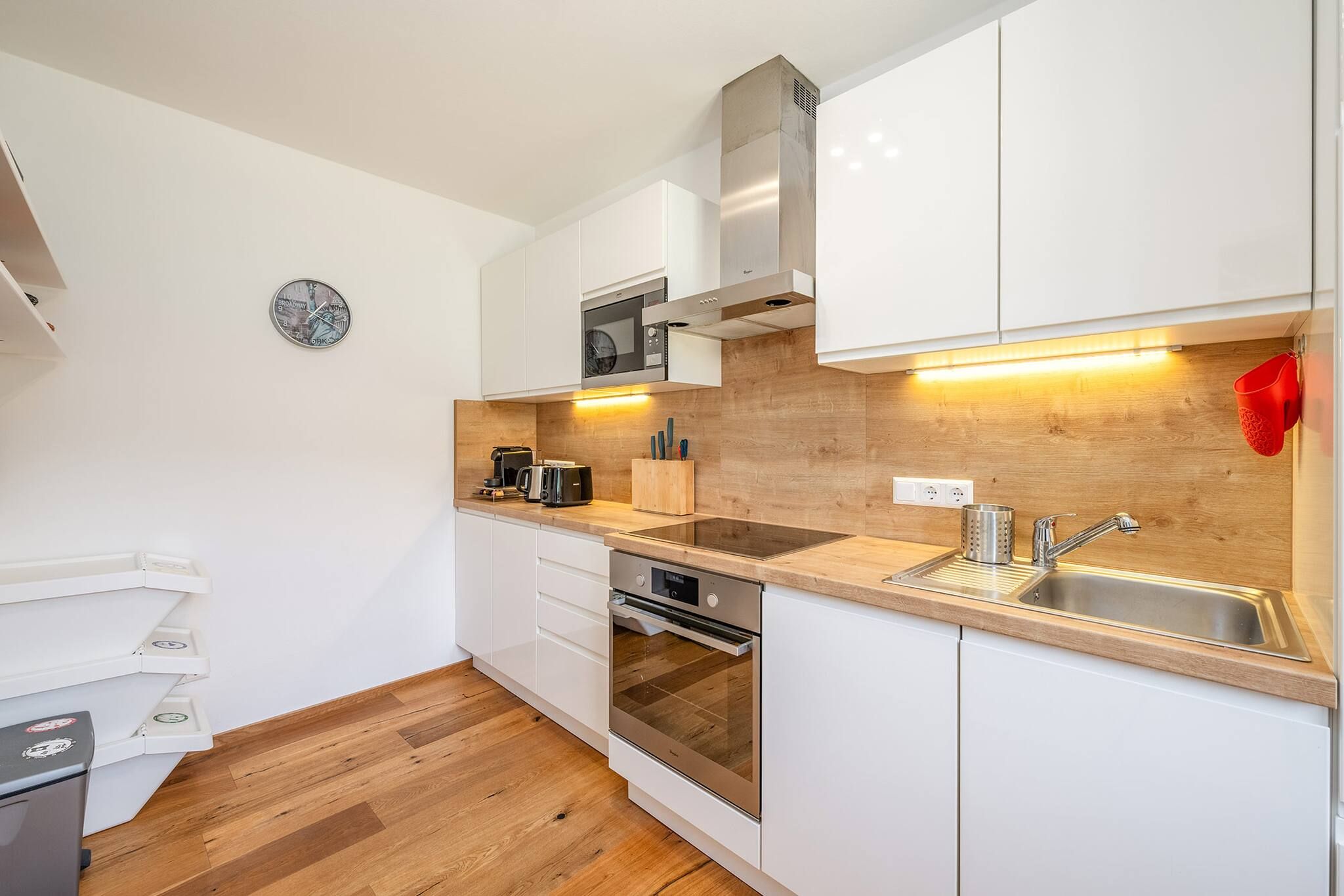 Cocina compacta con muebles blancos, extractor de acero inoxidable, microondas, tostadora y un lavamanos.