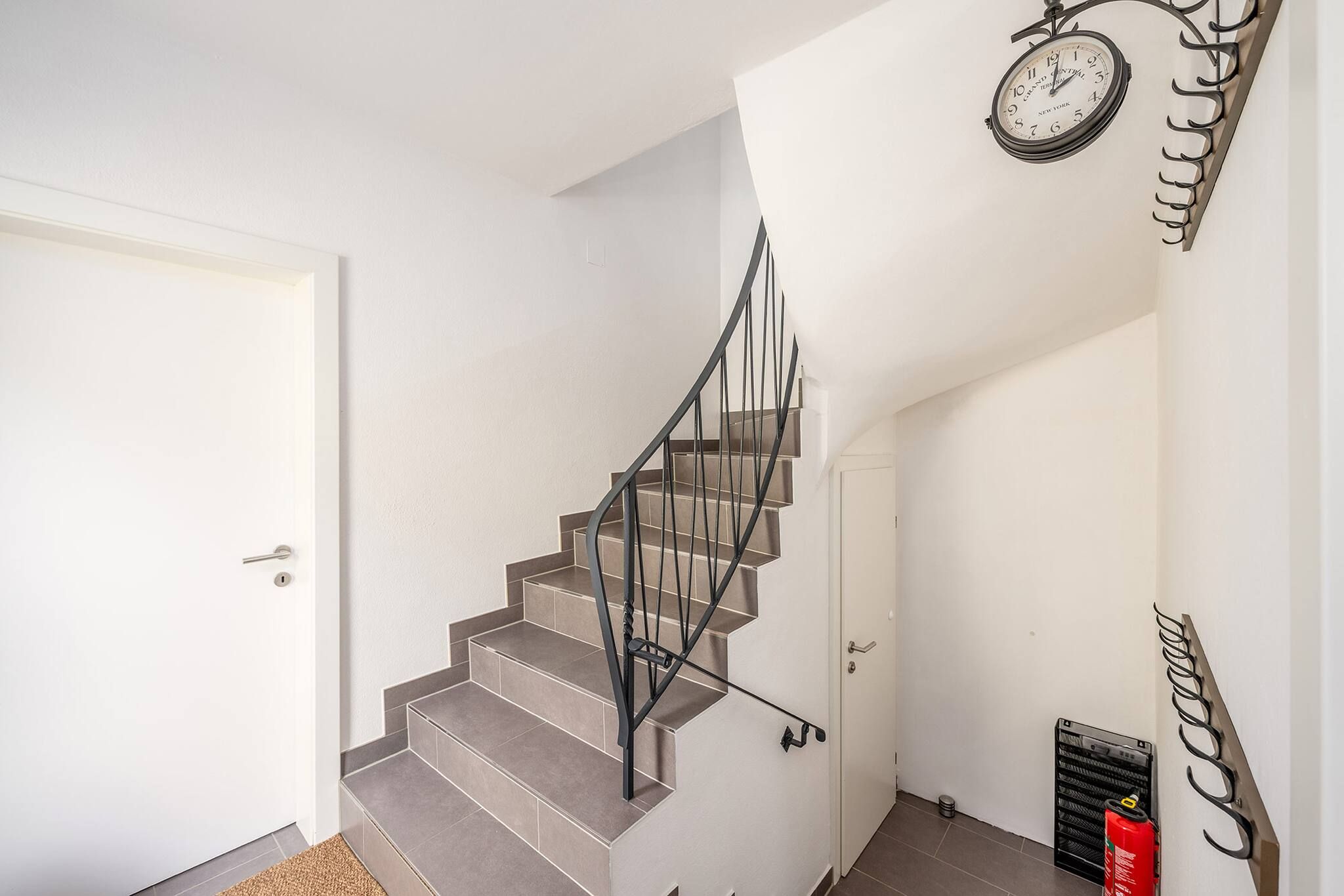 Eine Treppe mit Metallgeländer, einer weißen Tür und einer an der Wand befestigten Uhr.