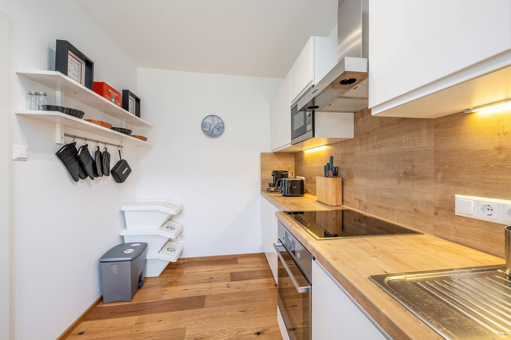 Cocina compacta con muebles blancos, encimera de madera, horno integrado y cafetera.