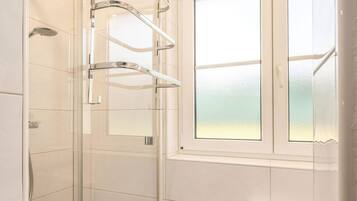 Ein modernes Badezimmer mit einer Duschkabine aus Glas, einem Fenster mit Milchglas und einem weißen Heizkörper.