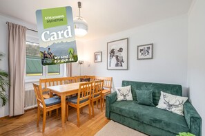 Ein gemütliches Wohnzimmer mit einem Holzesstisch, einem grünen Sofa und gerahmten Bildern an der Wand.