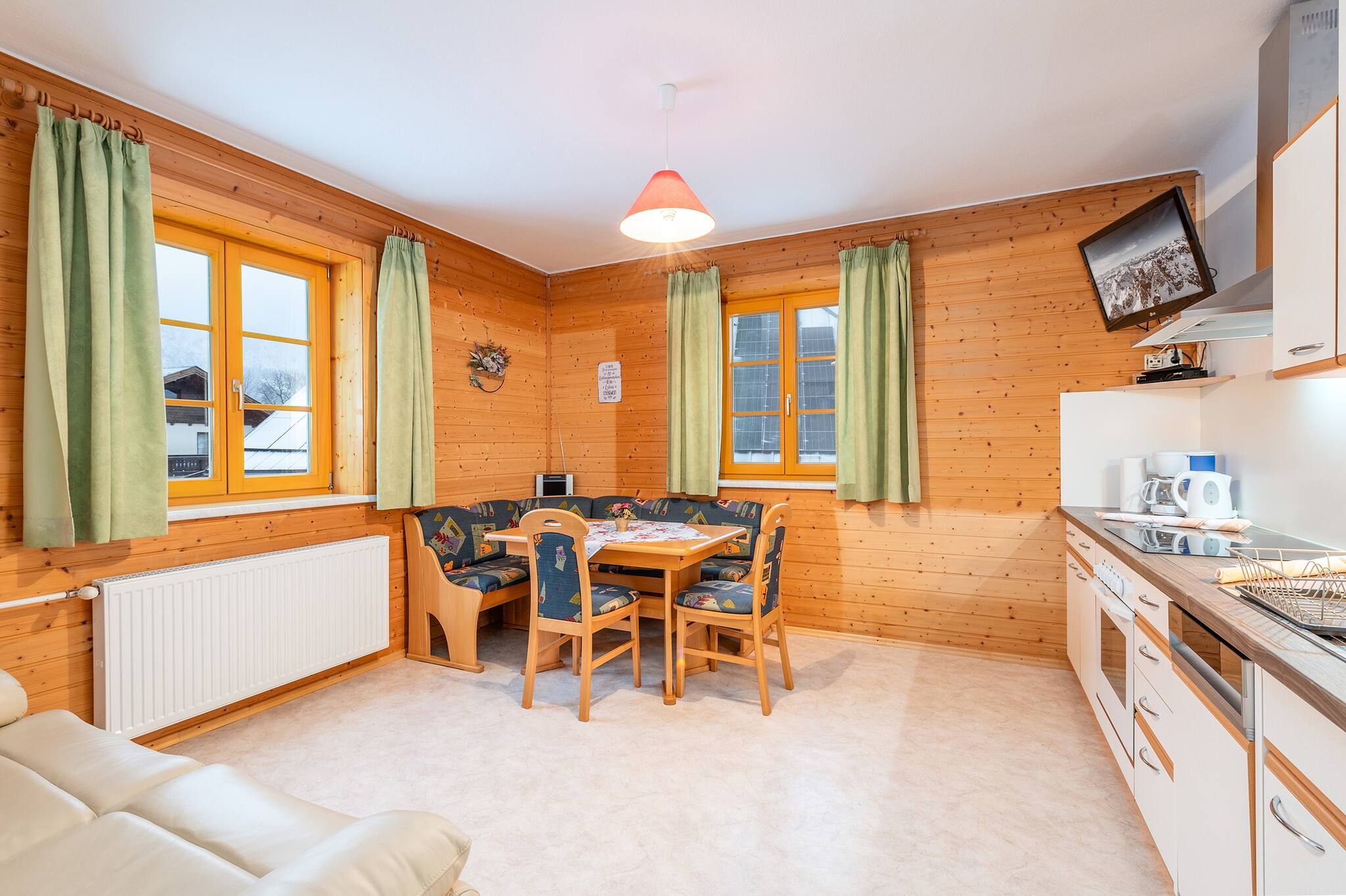 Ein gemütliches Zimmer mit Esstisch, Stühlen, einer Couch, einer Heizung, einem Fernseher und einer Küchenzeile.