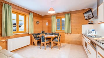 A cozy room with a dining table, chairs, a sofa, a radiator, a television, and a kitchen area.