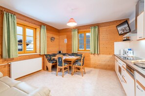 A cozy room with a dining table, chairs, a sofa, a radiator, a television, and a kitchen area.