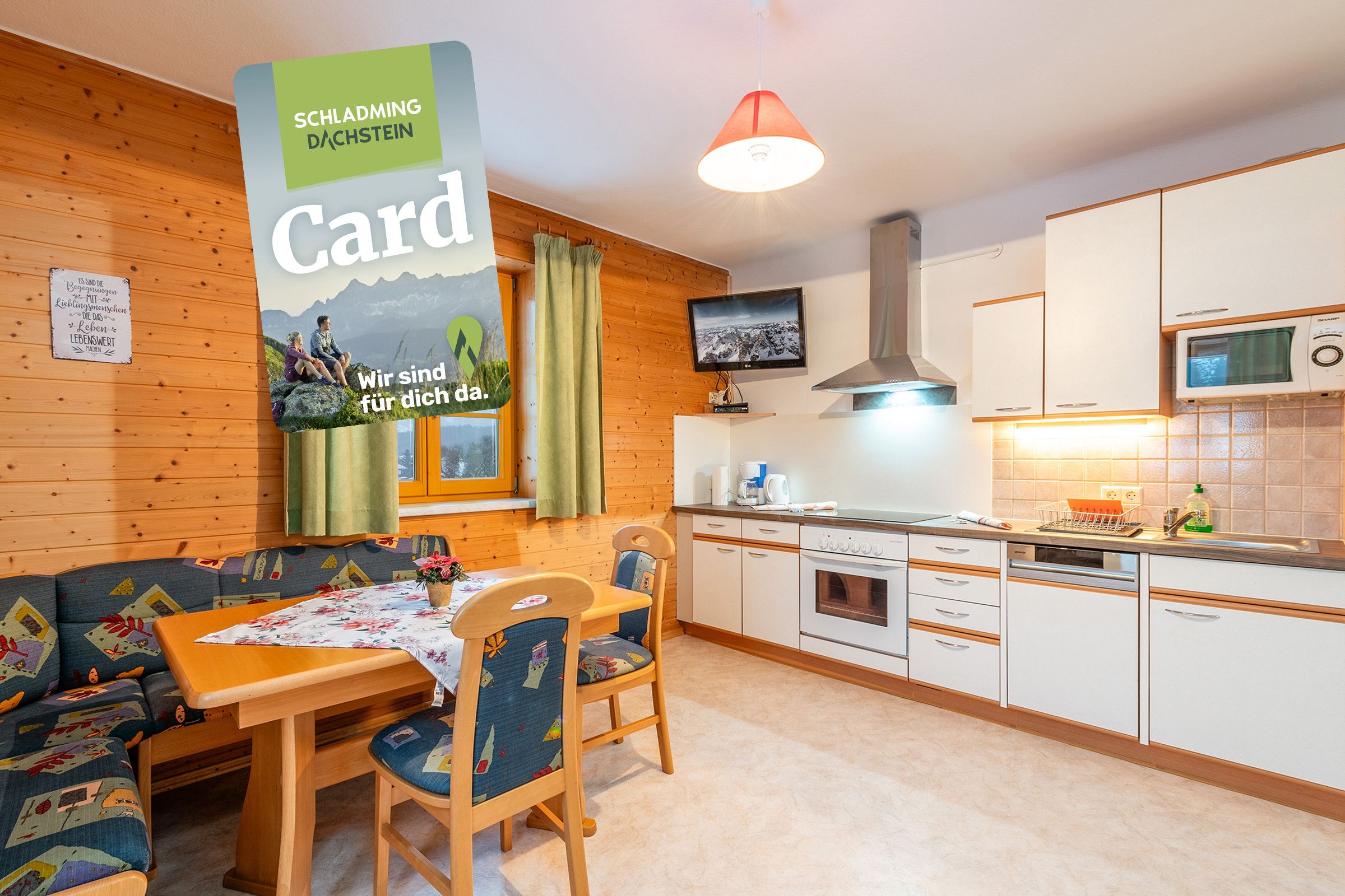 Un ambiente accogliente con arredamento in legno, un tavolo da pranzo con sedie, un divano, una cucina con mobili bianchi e una televisione a parete.