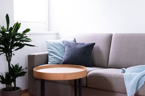 Ein Wohnzimmer mit einem grauen Sofa, zwei Kissen, einem runden Holztisch und einer Topfpflanze.
