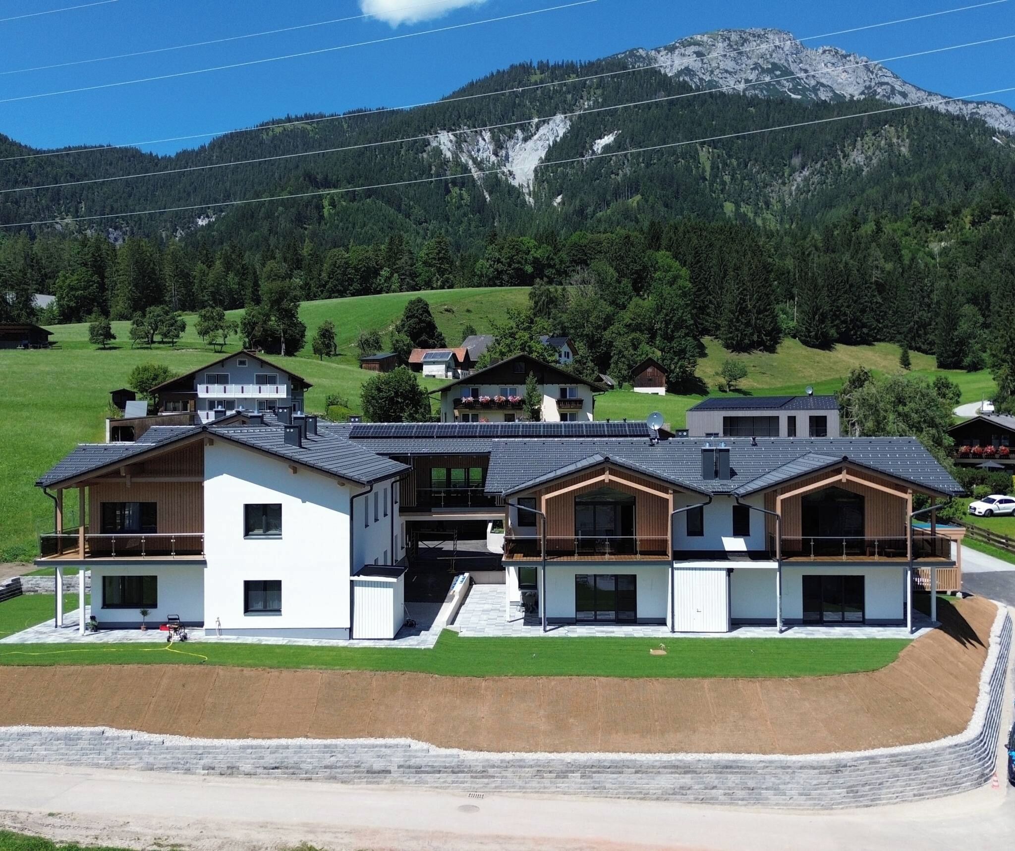 A modern multi-story building with a flat roof, surrounded by a green landscape and mountains in the background.