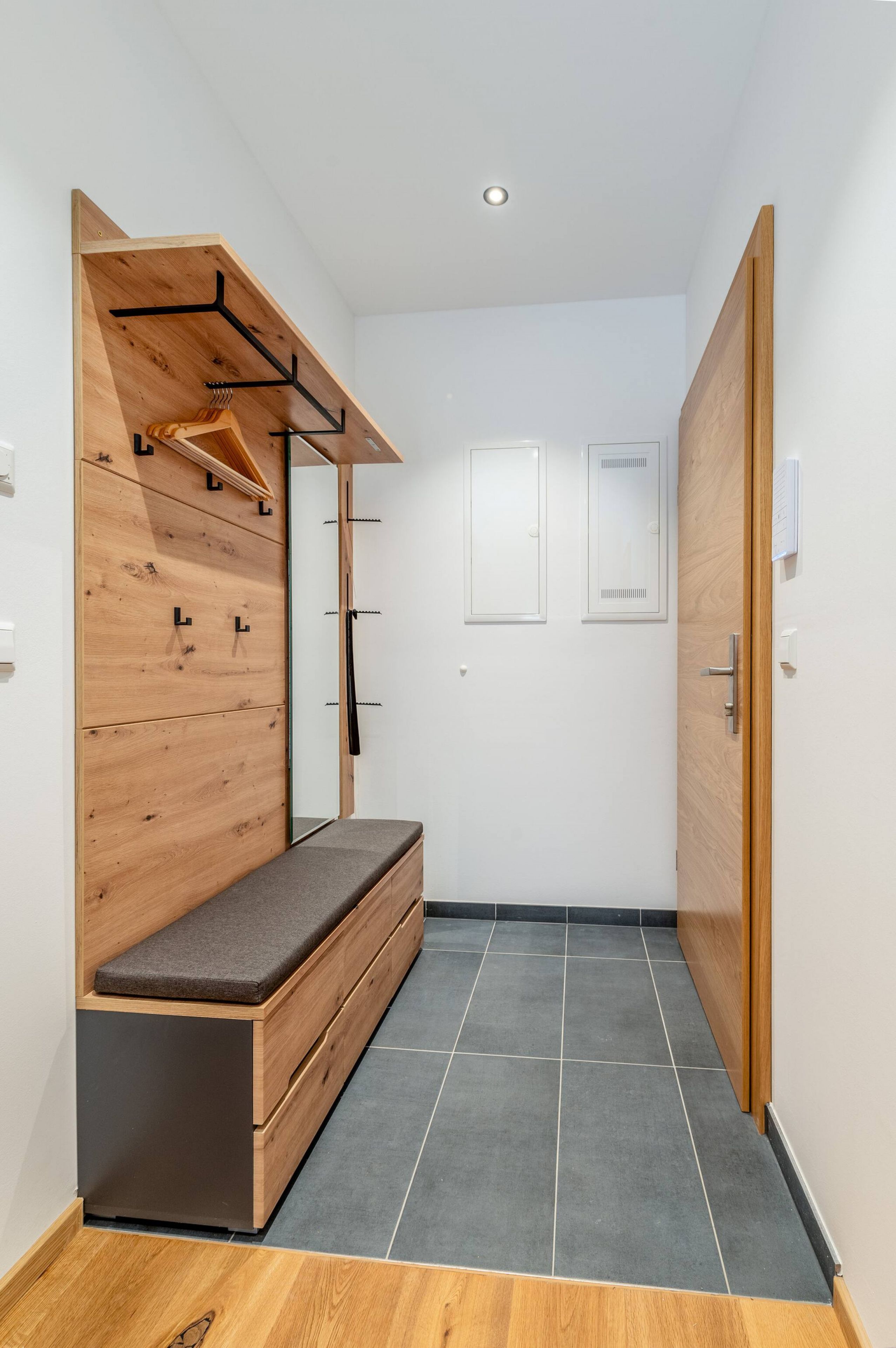 A modern, compact room with a built-in bench, a wooden wardrobe, and a door with a handle.
