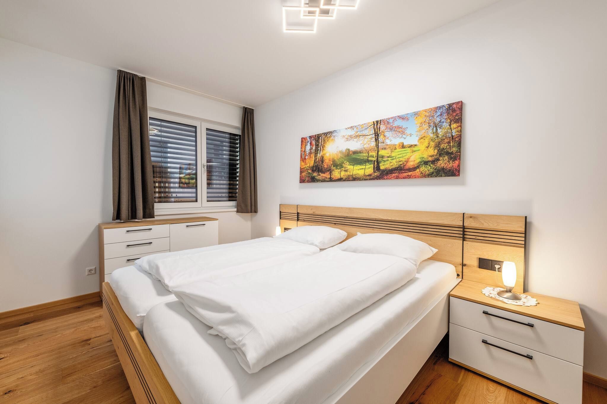 Un dormitorio con cama, mesitas de noche, una ventana con cortinas y un cuadro en la pared.