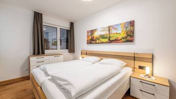Un dormitorio con cama, mesitas de noche, una ventana con cortinas y un cuadro en la pared.