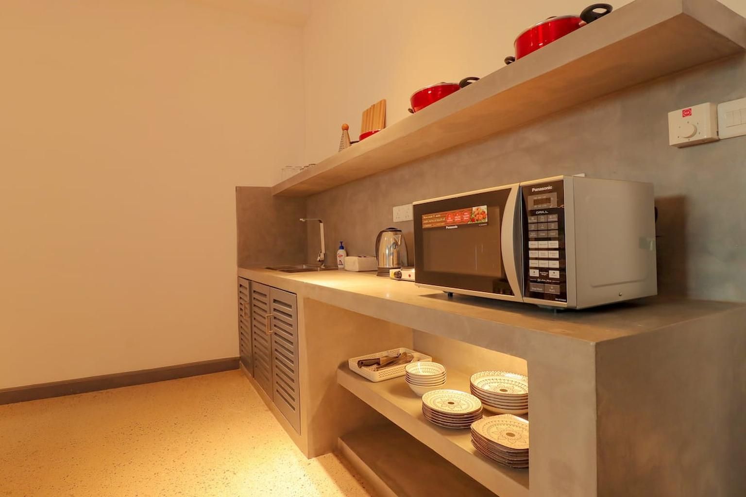 Une petite cuisine équipée d’un four à micro-ondes, d’une machine à café et d’une étagère où sont empilées des assiettes.