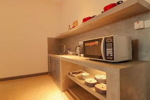 Eine Küchenzeile mit einer Mikrowelle, einer Kaffeemaschine und gestapelten Tellern auf einem Regal.