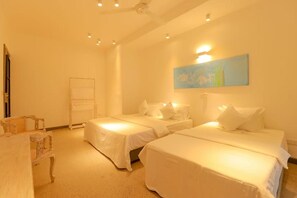 Ein Hotelzimmer mit zwei Betten, einem Sessel, einem Gemälde an der Wand und einem Deckenventilator.