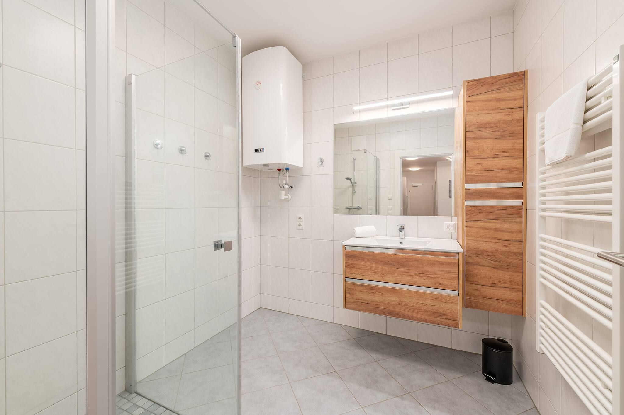Ein modernes Badezimmer mit Duschkabine aus Glas, einem Holzmöbelkorpus und einem weißen Handtuchhalter.