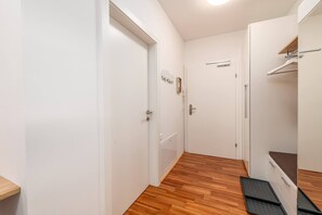 Ein schmaler Flur mit Holzdielen, weißen Wänden und einer Tür mit Griff.
