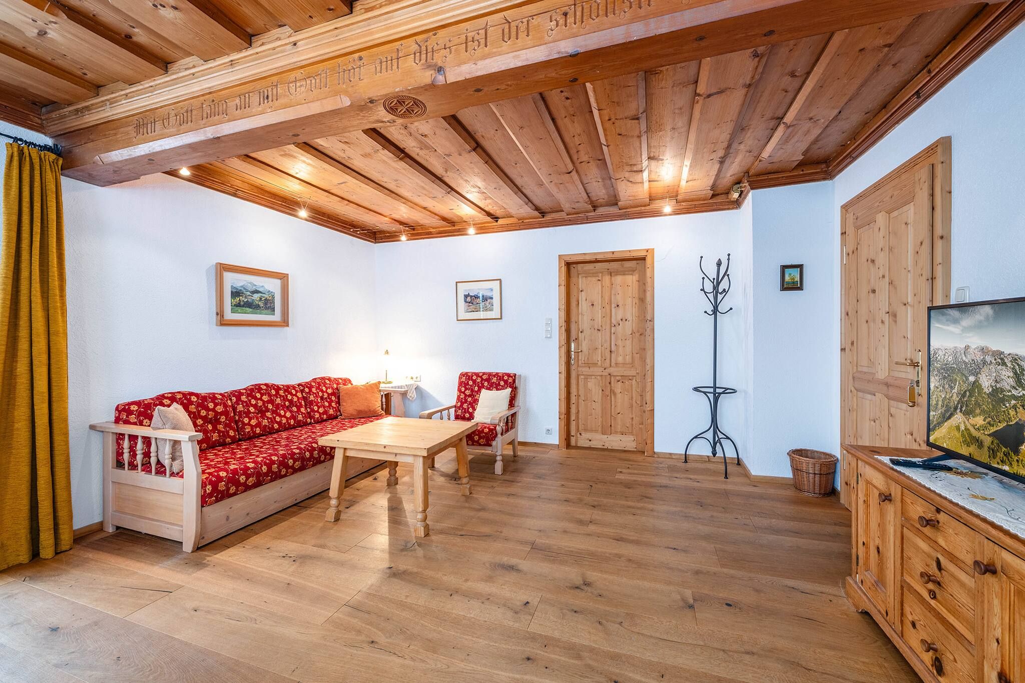 Ein gemütliches Zimmer mit Holzbalkendecke, einer Couch, einem Tisch und einem Fernseher.