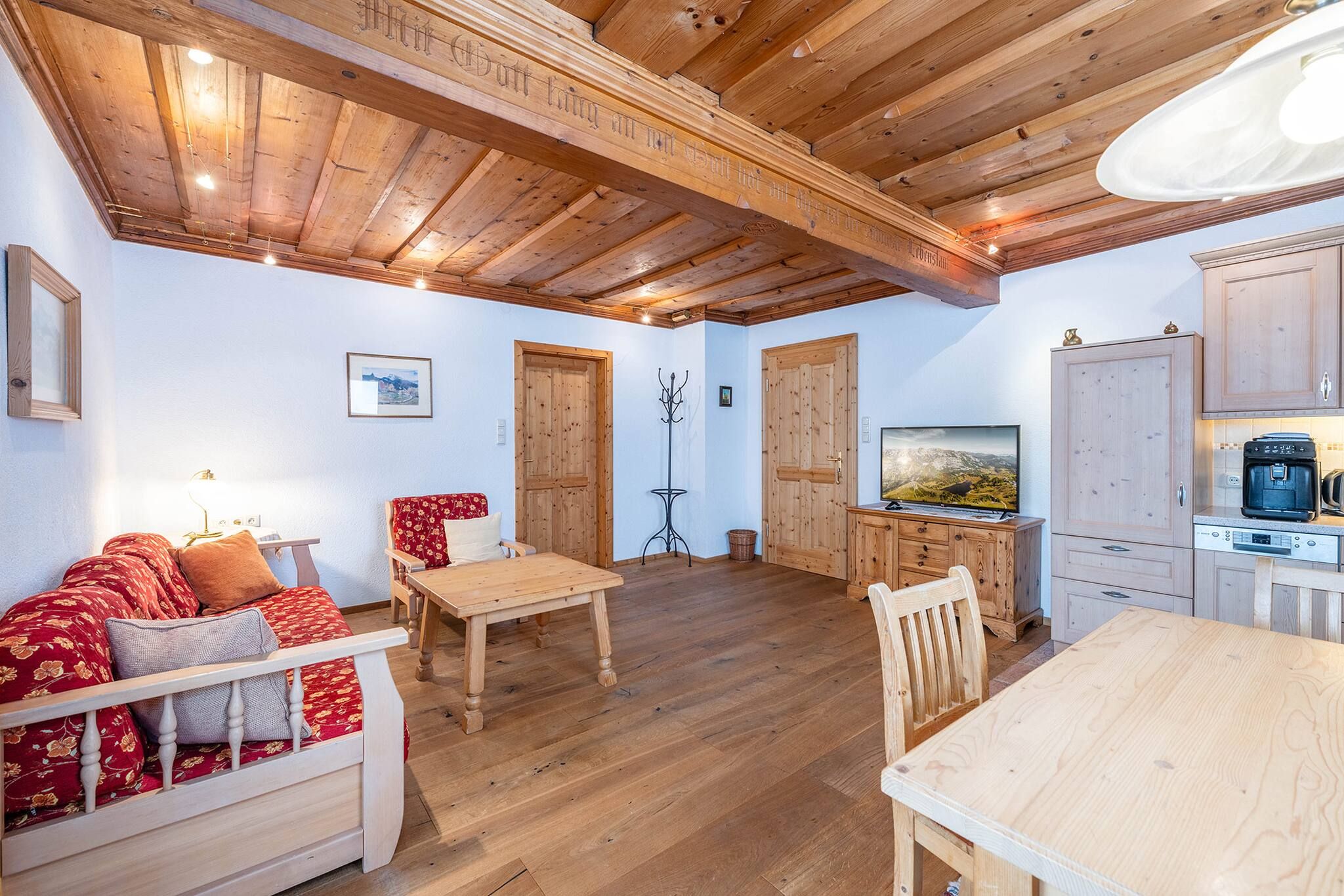 Ein gemütliches Wohnzimmer mit Holzmöbeln, einem Fernseher und einer Küchenzeile inklusive Schränken und Geräten.