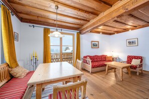A cozy room with a wooden ceiling, a dining table, a sofa, and a window with curtains.