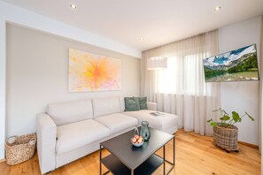 Un salon moderne avec un canapé, une table basse sur laquelle on a disposé des fruits, un tableau et un téléviseur panoramique.