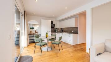 Une cuisine moderne avec des meubles blancs, un coin repas doté d’une table ronde et de chaises, et un canapé dans l’espace salon.