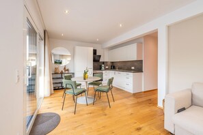 Une cuisine moderne avec des meubles blancs, un coin repas doté d’une table ronde et de chaises, et un canapé dans l’espace salon.
