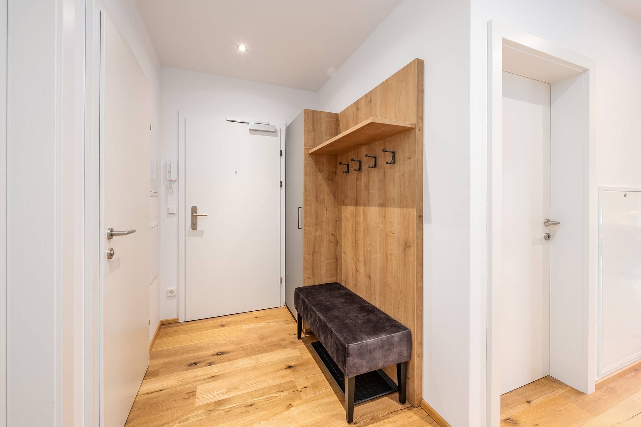 A hallway with wooden flooring, a bench, and a wooden wall with hooks.
