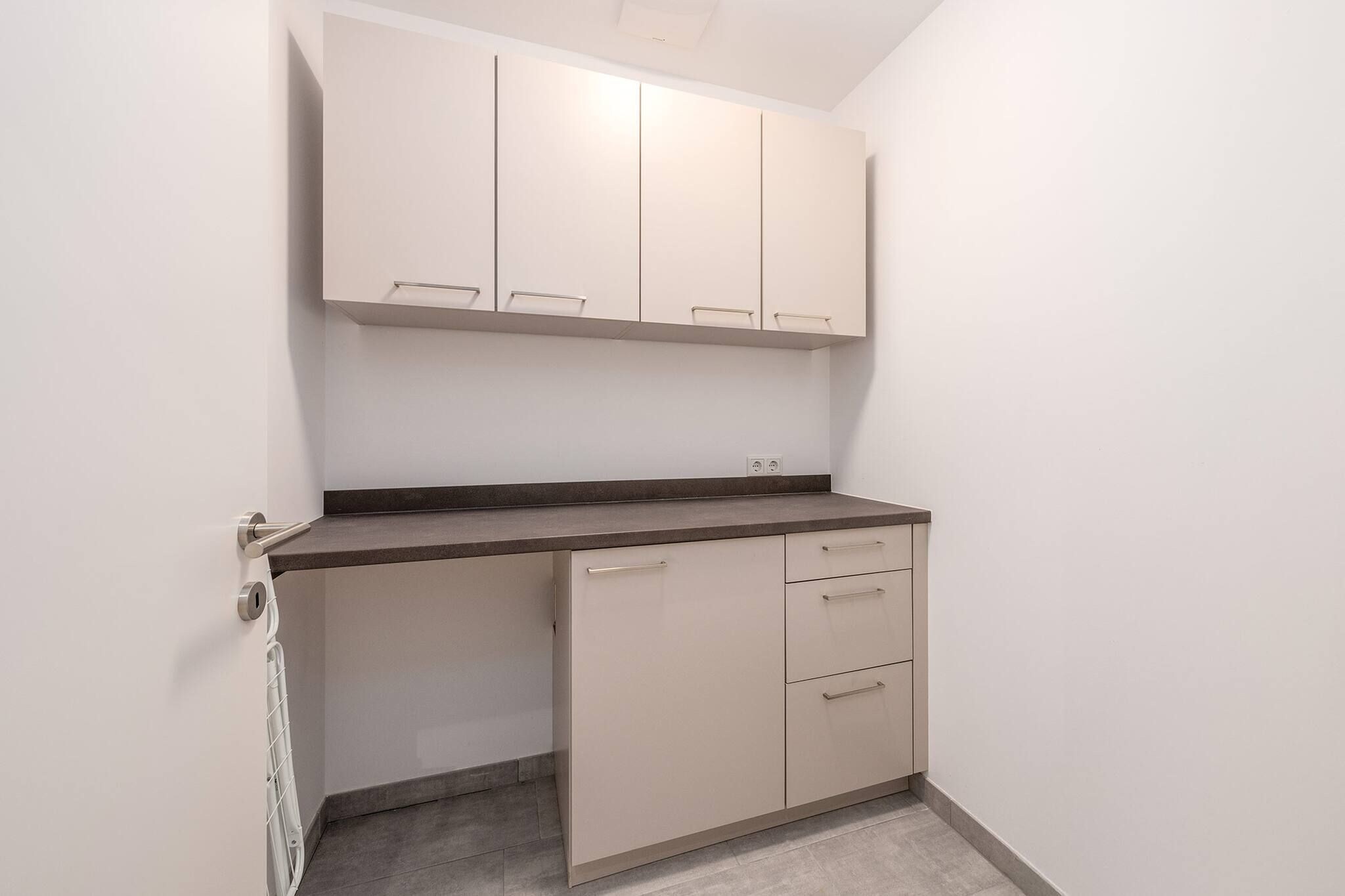 Een compacte kitchenette met een aanrecht, kastjes en een deur.