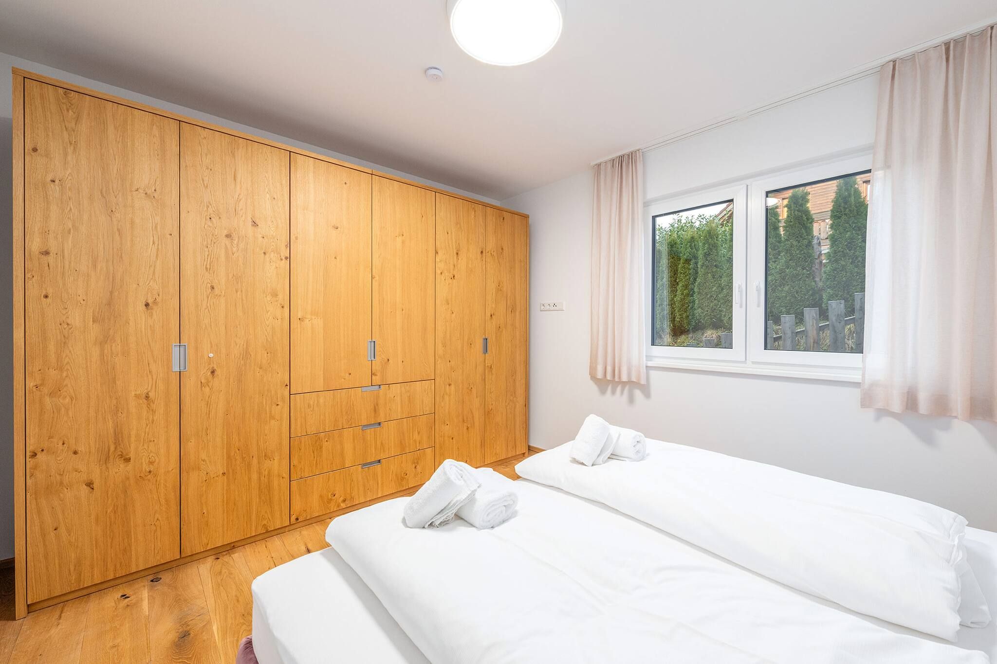 A bedroom with a large wooden wardrobe, two beds, and a window with curtains.