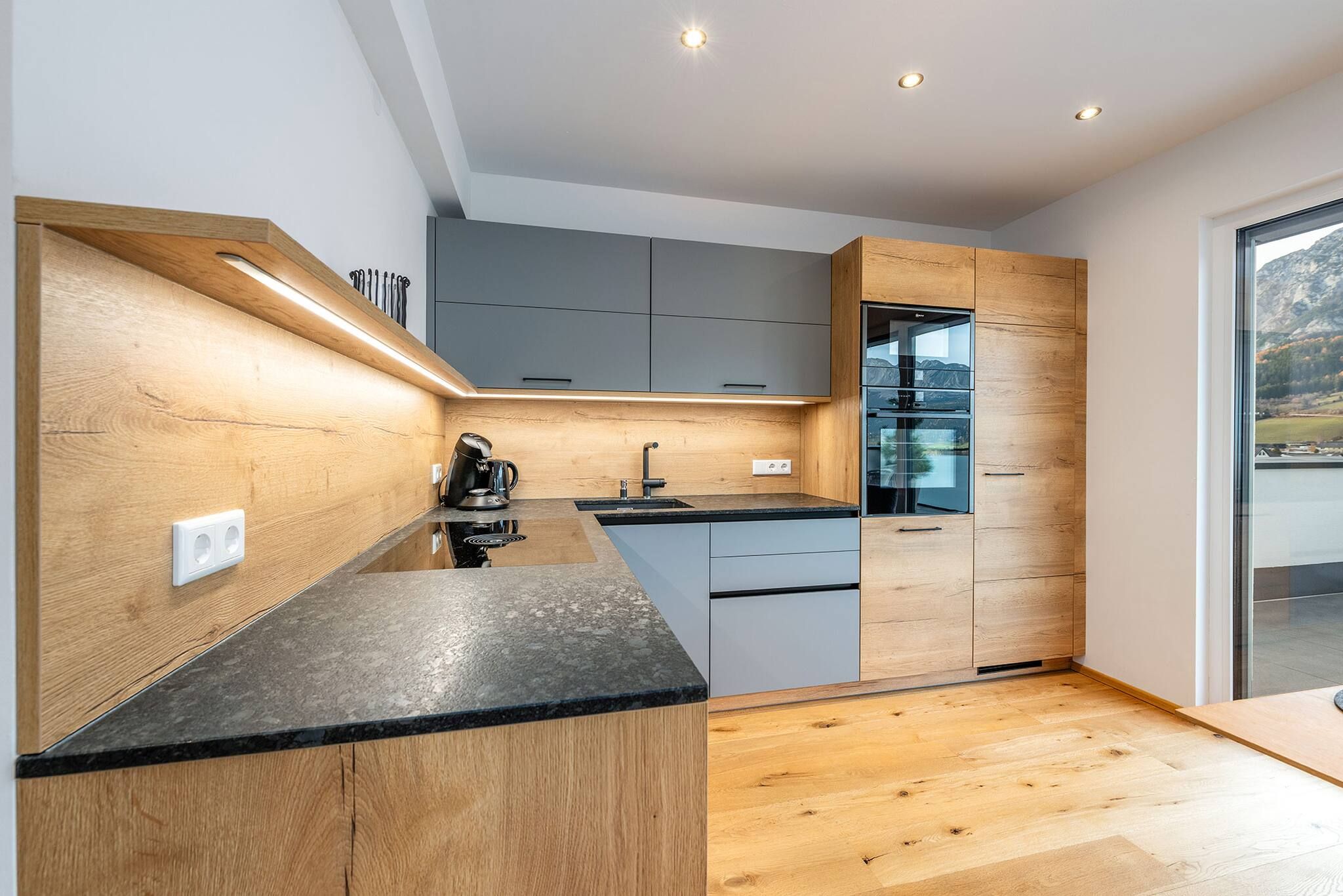 Una cocina moderna con muebles de madera, horno empotrado y un amplio ventanal con vistas al exterior.