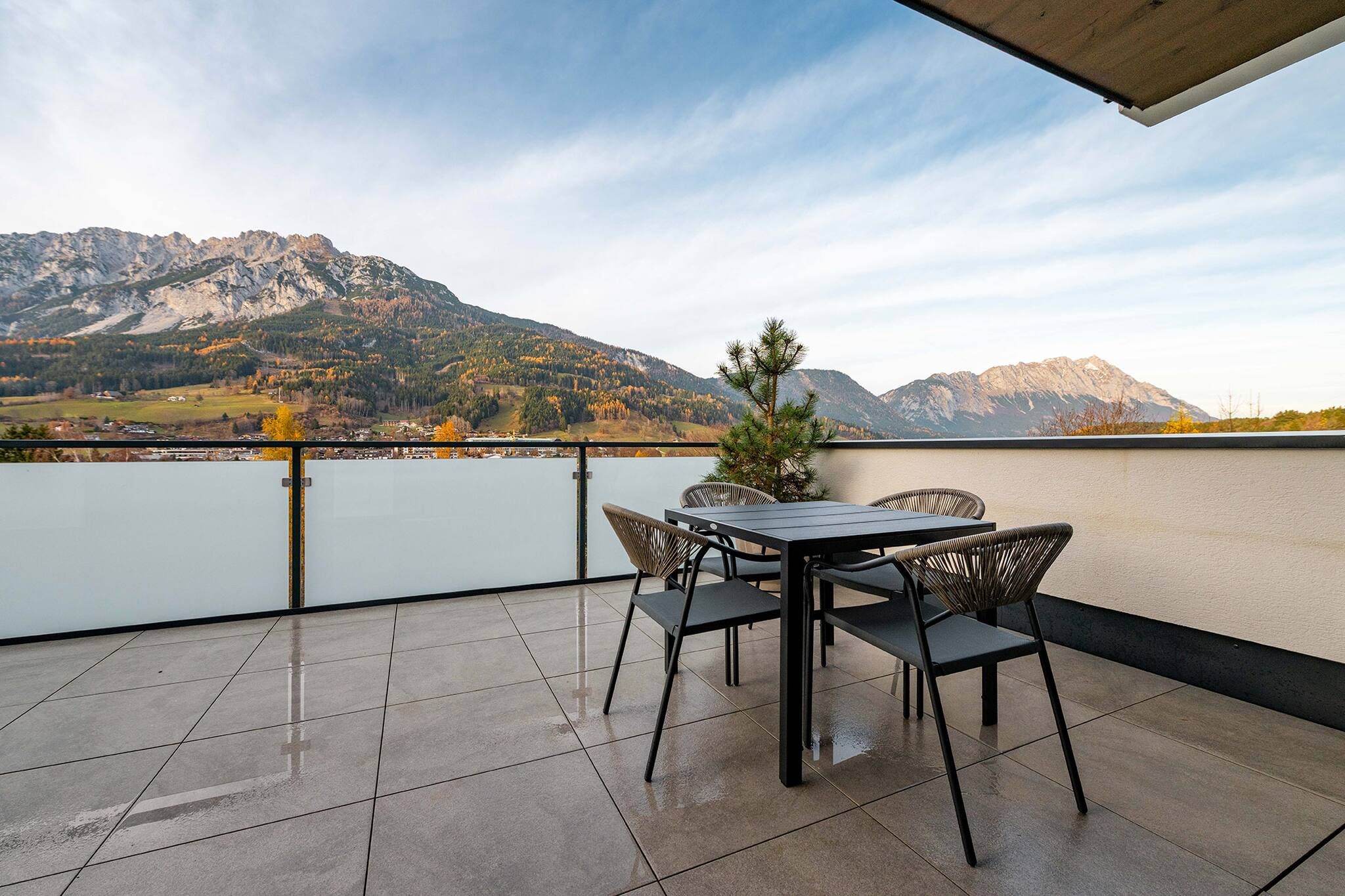 A terrace with a table and chairs, overlooking a lake and mountains.