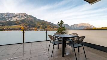 A terrace with a table and chairs, overlooking a lake and mountains.