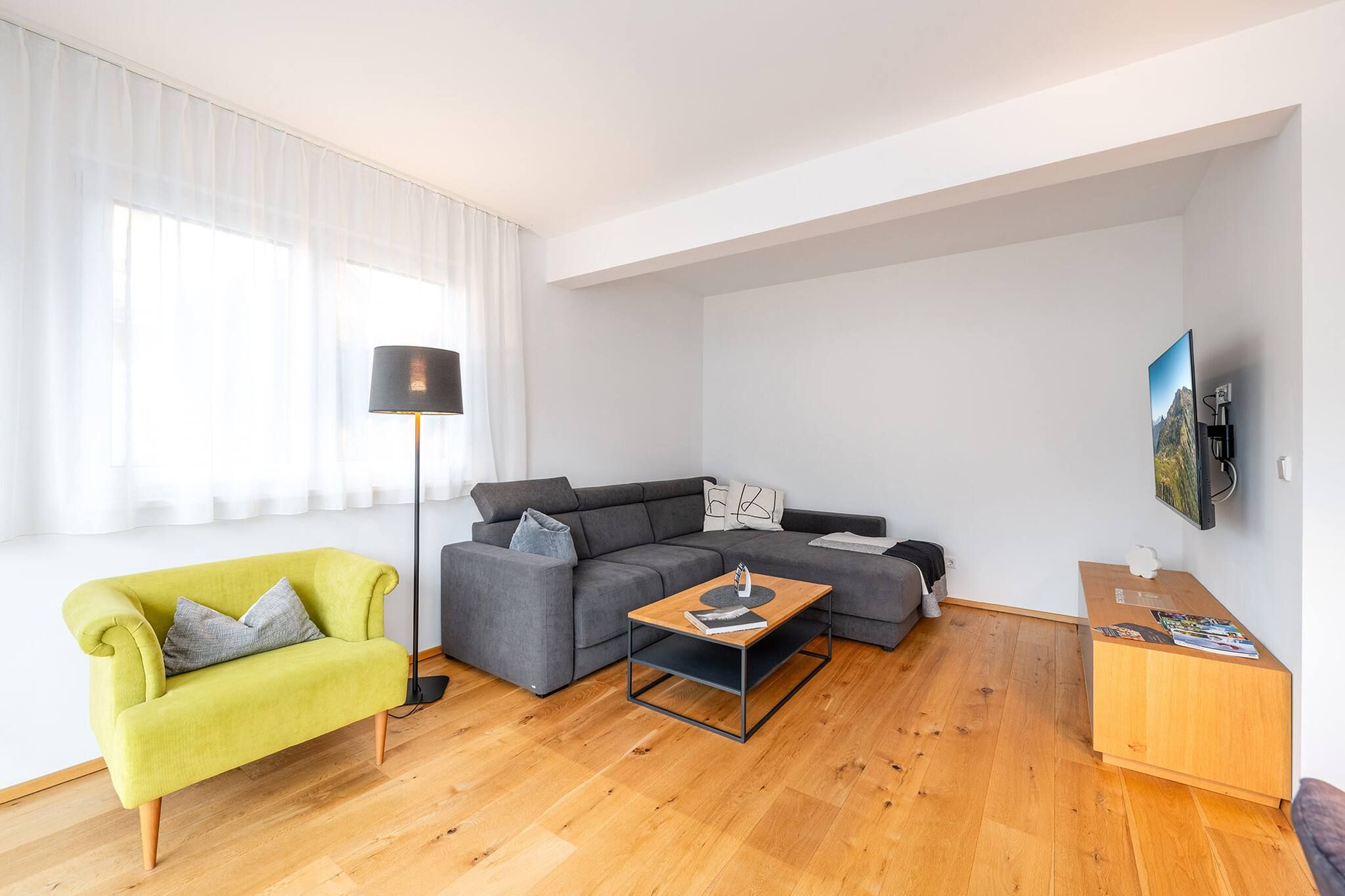 Ein modernes Wohnzimmer mit einer Couch, einem Couchtisch, einer Lampe und einem an der Wand befestigten Fernseher.