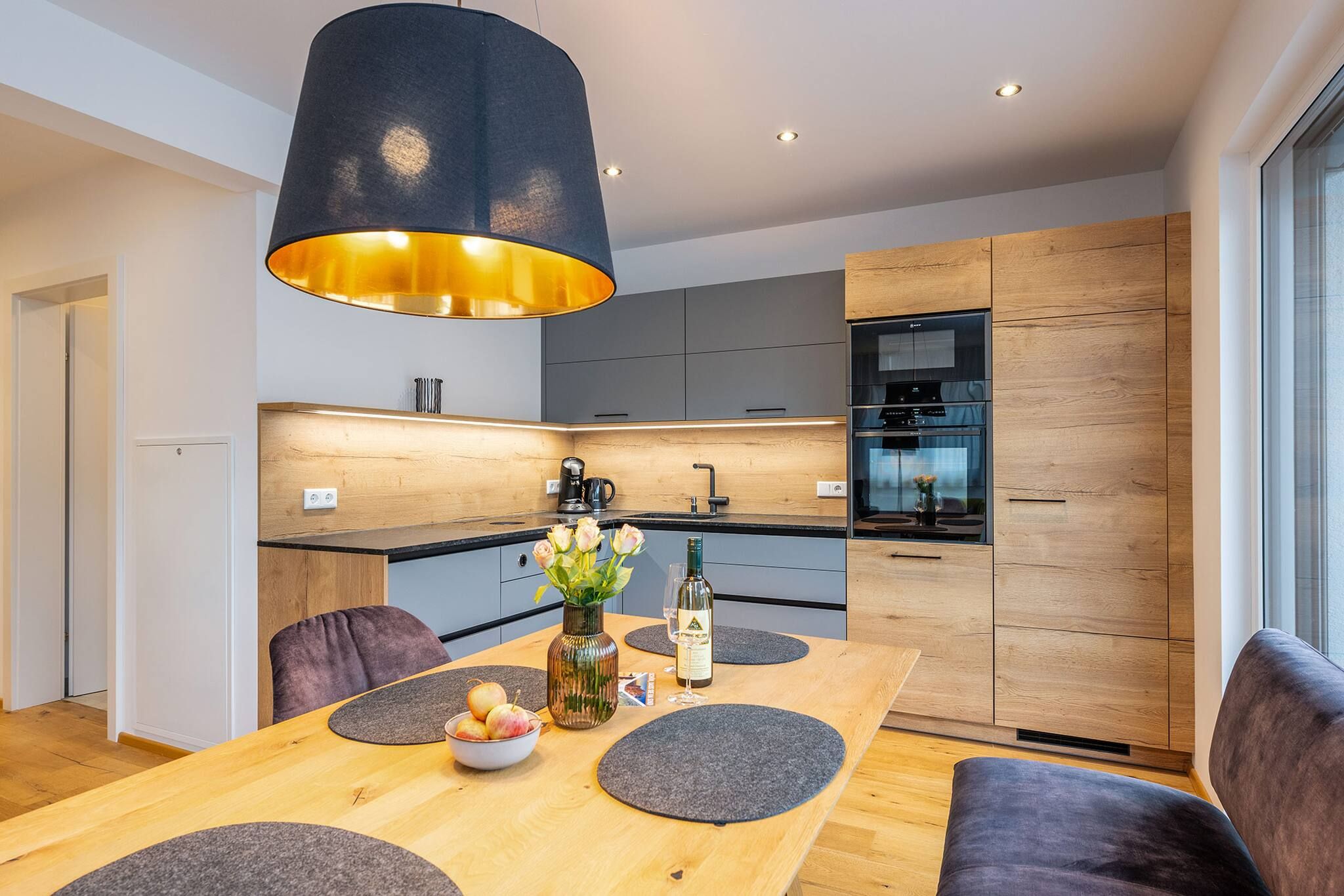 Una cocina moderna con una mesa de comedor de madera, individuales grises y un florero con flores.